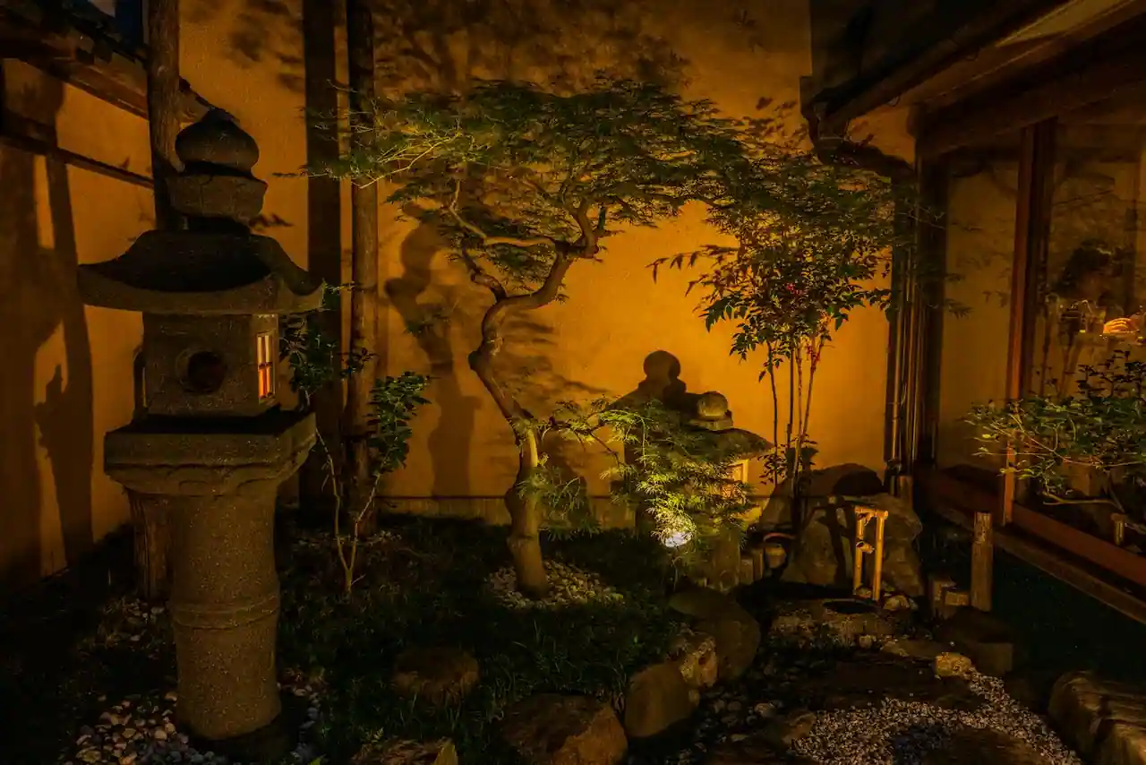 Jardin japonais avec érable rouge, lanterne en pierre, mousses au sol et gravier ratissé autour d'un rocher