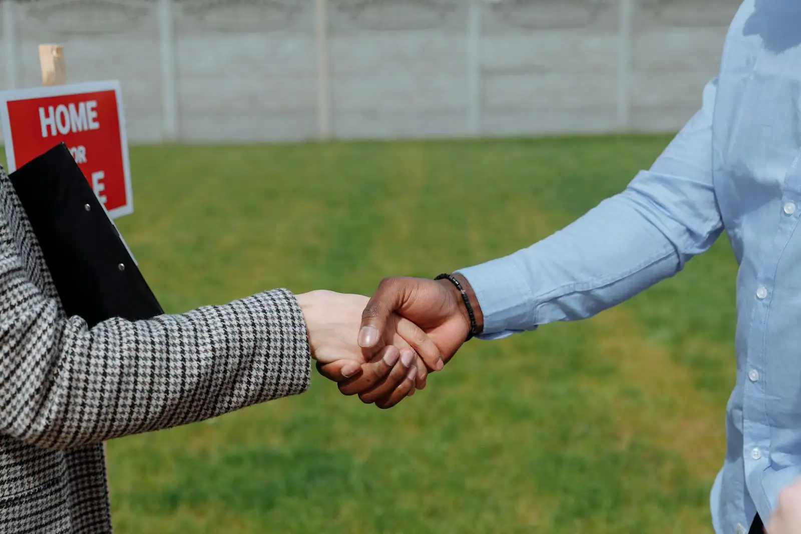 Poignée de main entre deux personnes devant une maison en pierre avec un panneau à vendre
