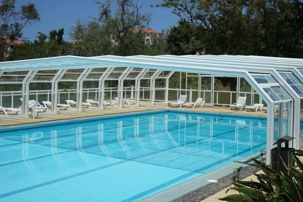 Abri de piscine bas vitré couvrant un bassin dans un jardin ensoleillé