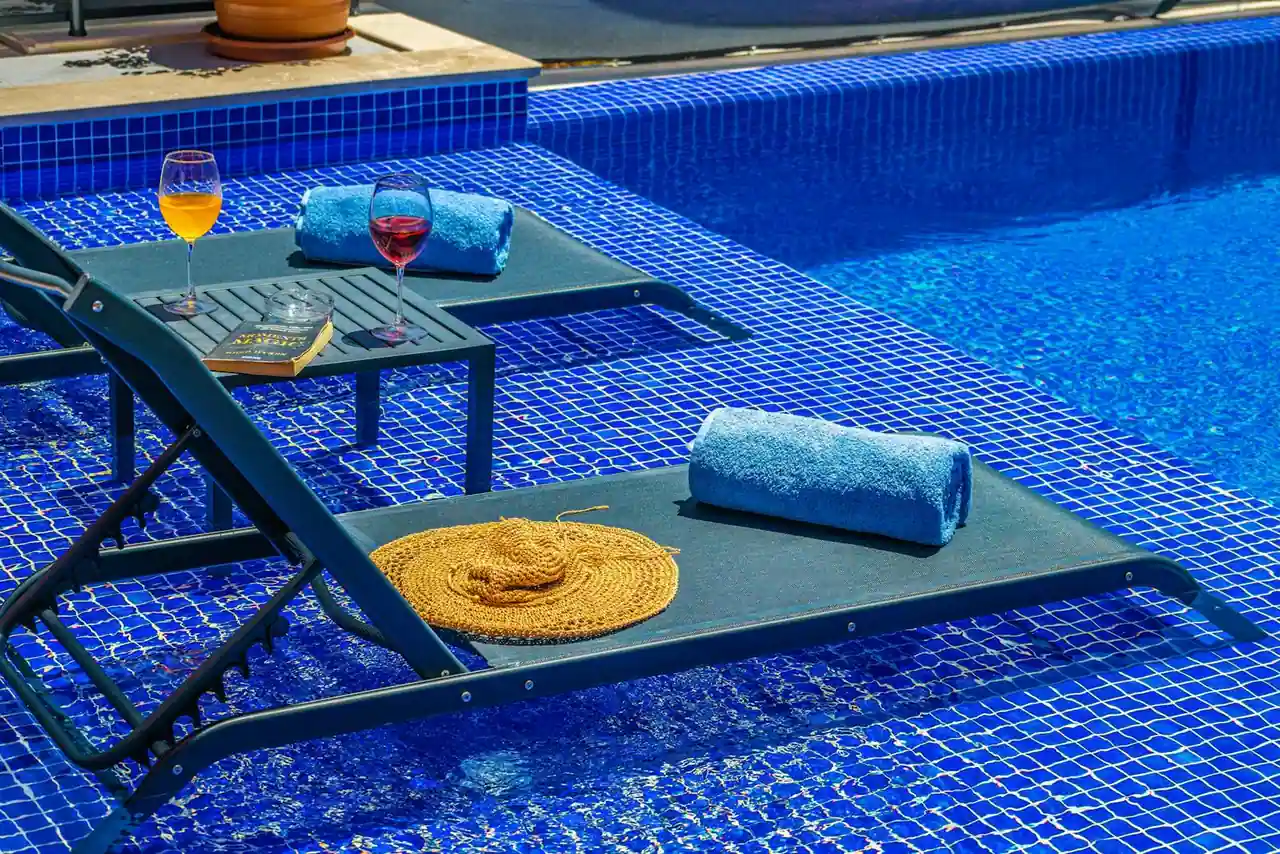 Transats et serviettes sur une plage de piscine carrelée de mosaïque bleue, au bord du bassin