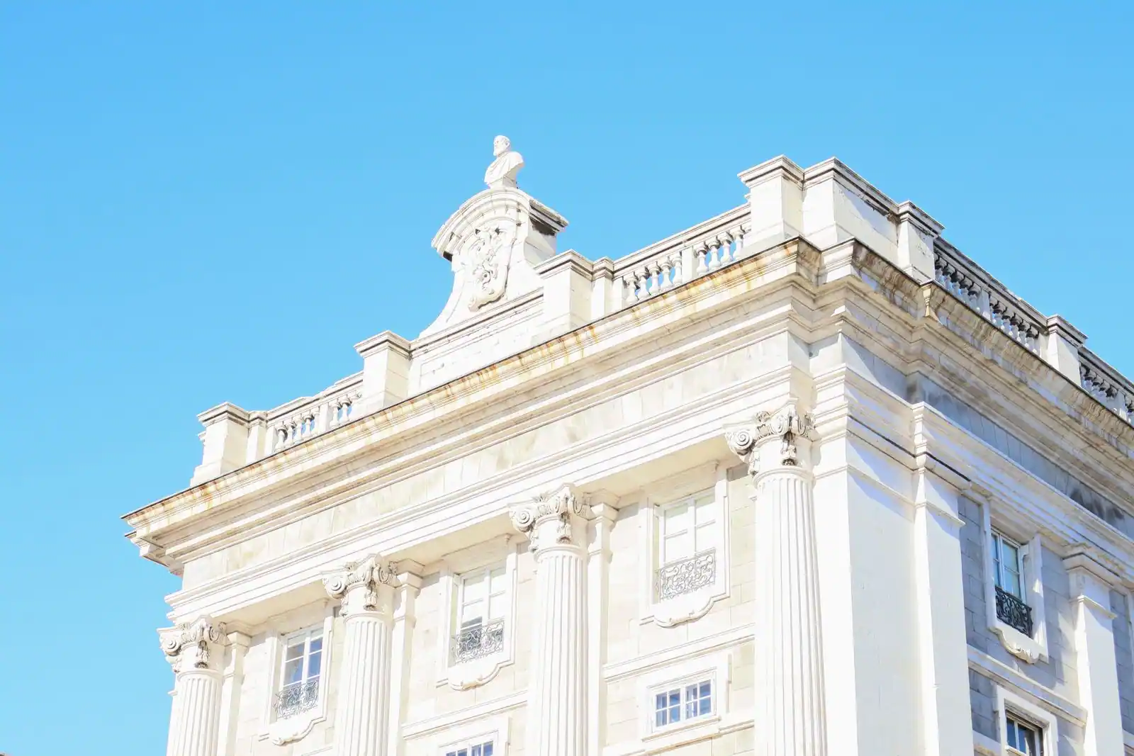 Façade en pierre claire d'un bâtiment institutionnel néoclassique orné de colonnes, sous un ciel bleu