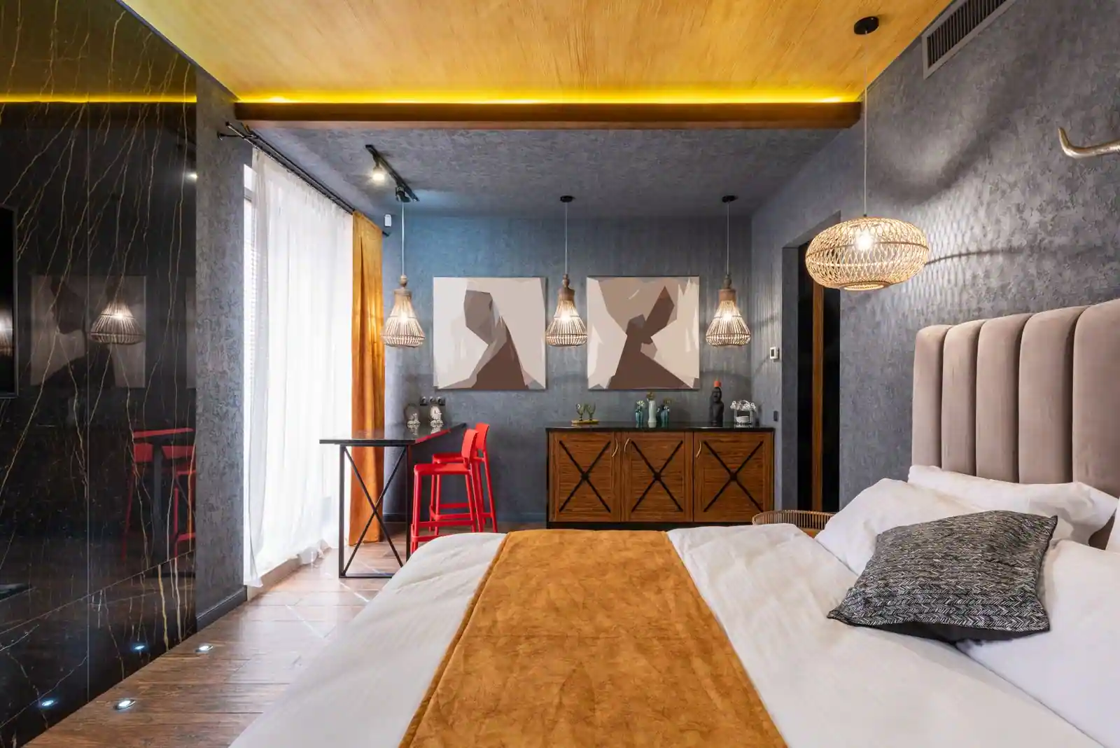 Chambre design aux murs sombres et mur de marbre noir, lit aux tons chauds et suspensions en rotin