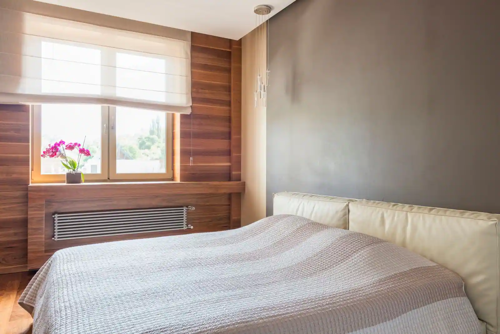 Chambre à coucher moderne avec habillage mural en bois clair, lit aux teintes neutres et orchidée à la fenêtre.