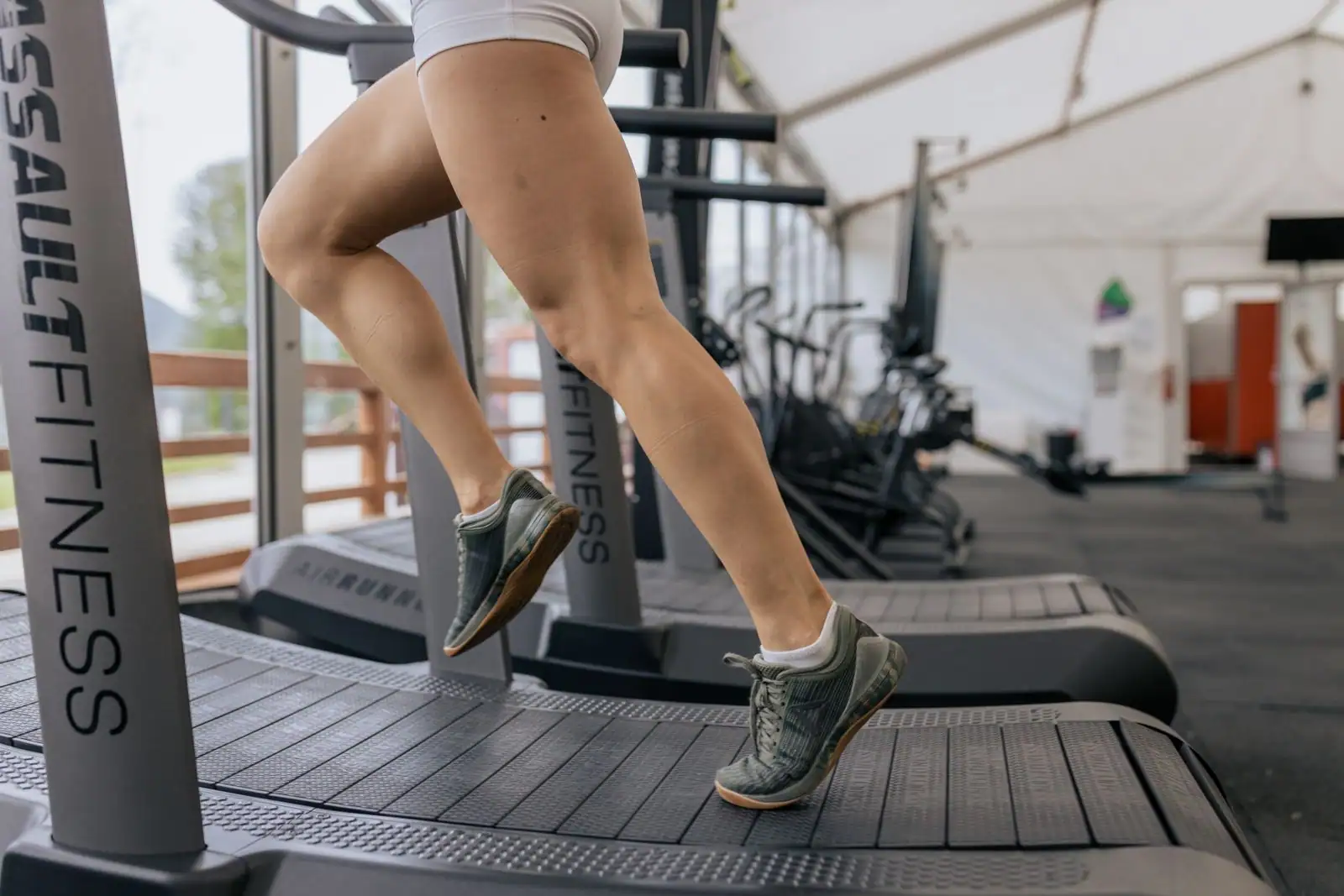 Jambes d'une personne courant sur un tapis de course en salle de sport, illustrant l'entraînement d'endurance en intérieur.