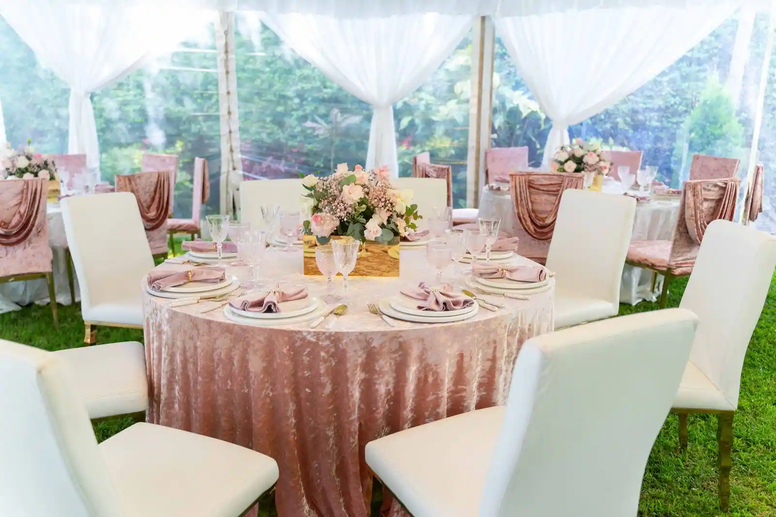 Tables dressées et chaises blanches sous une tente de réception décorée pour un événement