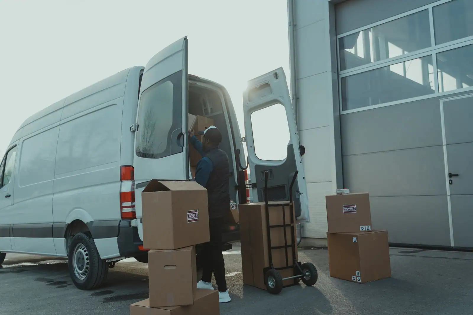 Un utilitaire blanc aux portes arrière ouvertes, chargé de cartons à l'aide d'un diable.