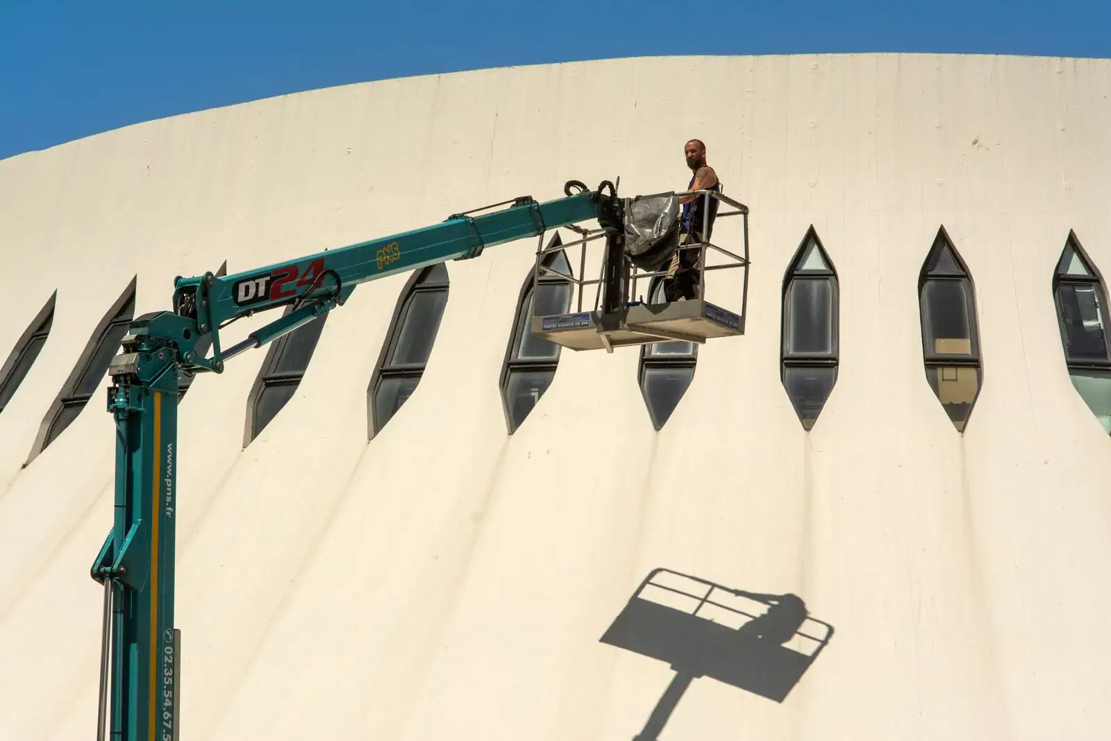 Ouvrier travaillant en hauteur depuis une nacelle élévatrice déployée le long de la façade d'un bâtiment.