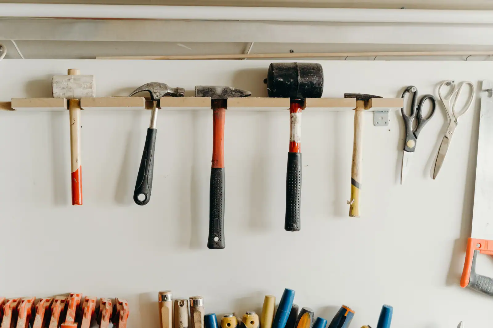 Outils de bricolage — marteaux, maillet, ciseaux et scie — accrochés en rangée sur un support mural