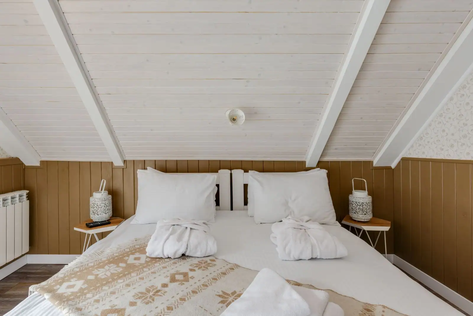 Chambre à coucher chaleureuse avec lit en bois clair, linge blanc et coussins, baignée de lumière naturelle.