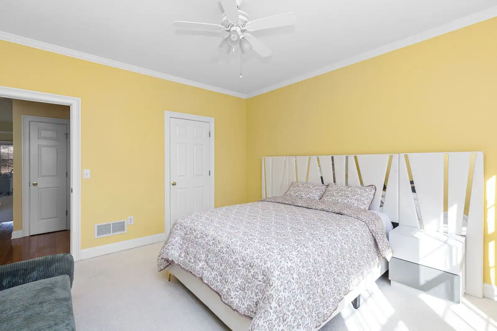 Chambre aux murs jaune pâle et mobilier blanc, lit habillé de textiles clairs sous une lumière naturelle douce.