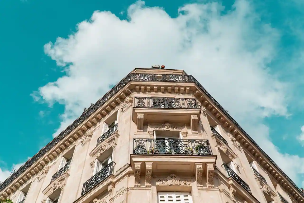 Façade en pierre d'un immeuble haussmannien parisien, aux balcons en fer forgé, sous un ciel clair.