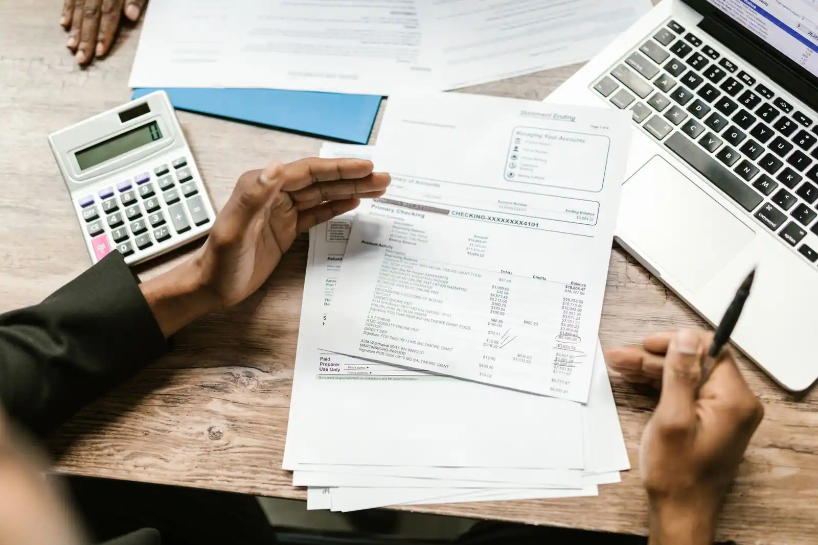 Personne examinant des relevés et documents comptables avec une calculatrice, évoquant l'examen des comptes.