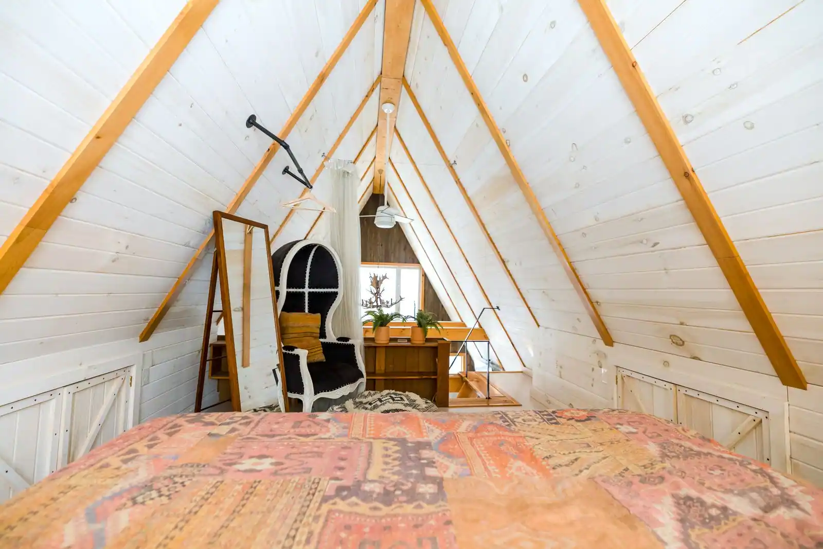 Chambre aménagée sous les combles : plafond en forte pente, poutres apparentes en bois et lit sous les rampants.
