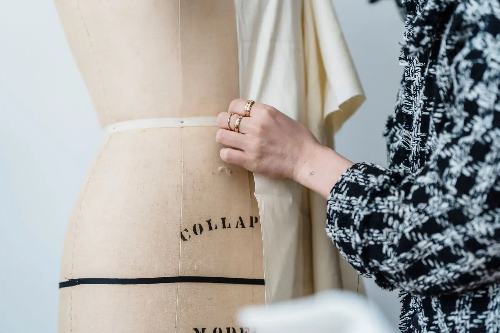 Main d'une couturière ajustant un ruban sur un mannequin de couture toilé, dans un atelier — le geste du sur-mesure.