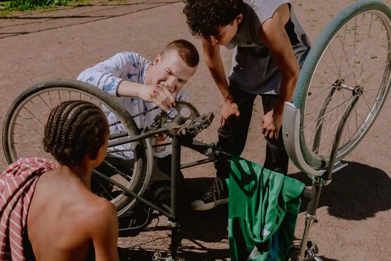 Des jeunes réparent un vélo retourné dans la rue, chaîne et roue arrière bien visibles.