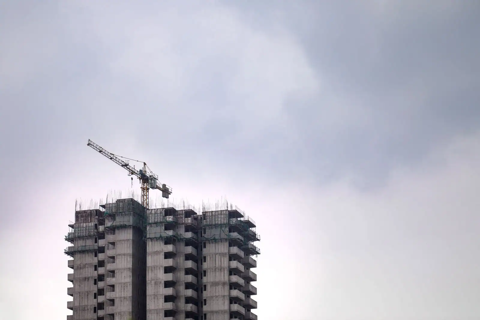 Immeuble en construction avec sa structure en béton et une grue de chantier, sous un ciel couvert.