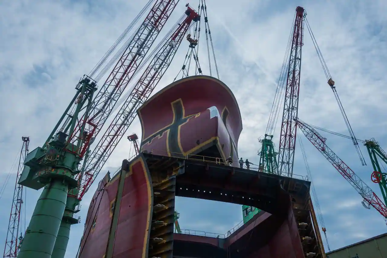 Bloc de coque d'un navire en construction hissé par des grues portiques dans un chantier naval