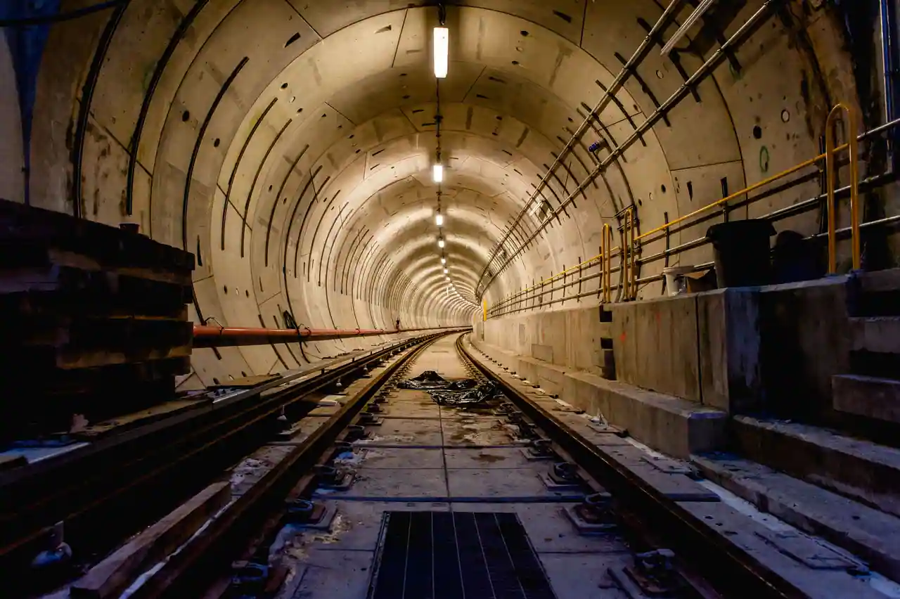Intérieur d'un tunnel ferroviaire souterrain au revêtement de béton segmenté, voie s'enfonçant au loin.
