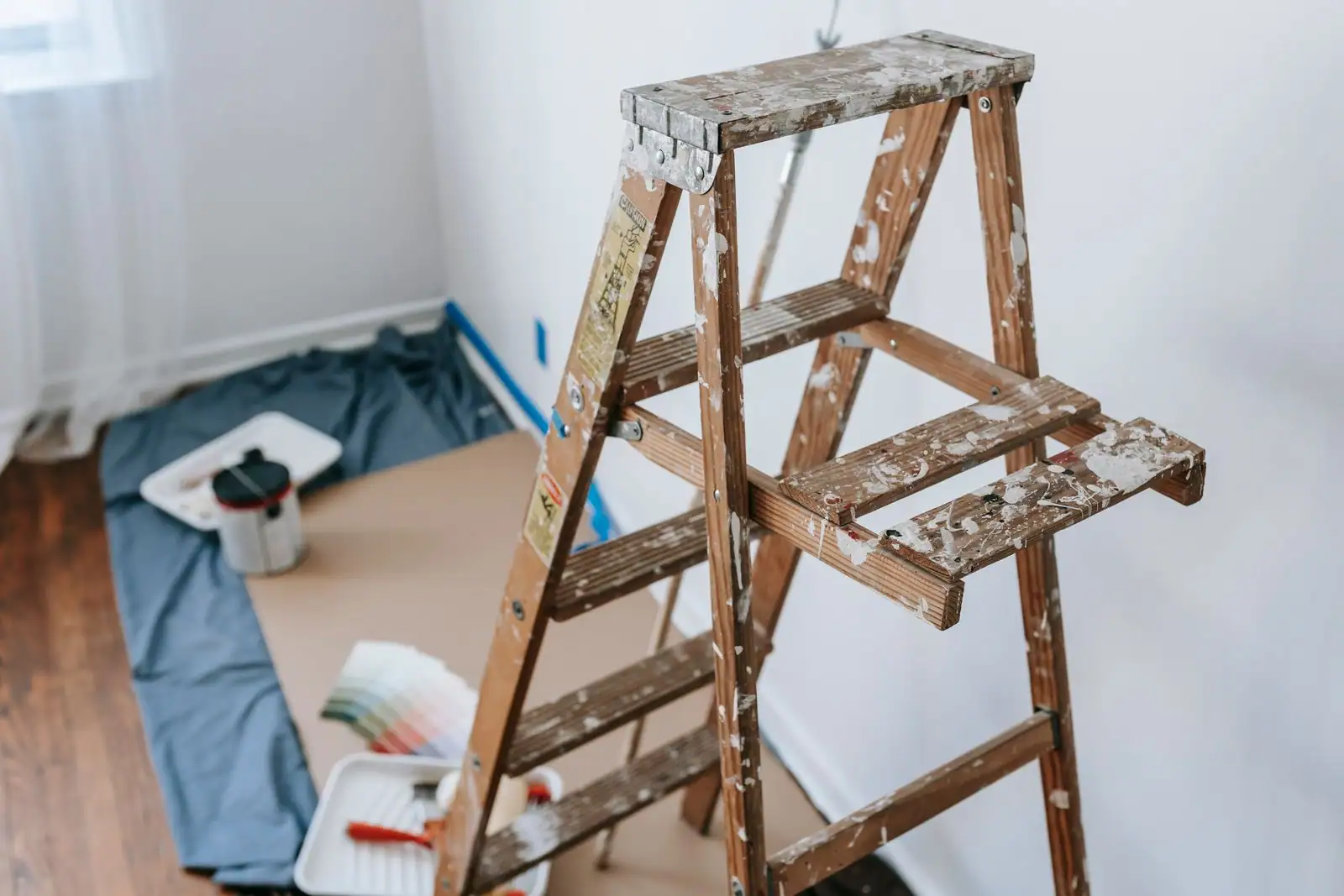 Escabeau taché de peinture, bac à rouleau et nuancier dans une pièce de maison en rénovation.