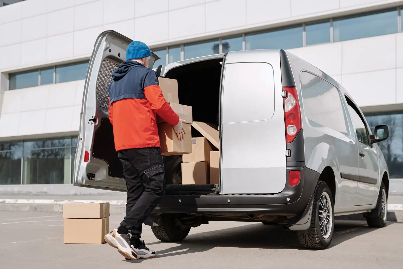 Personne chargeant des cartons dans un fourgon utilitaire aux portes arrière ouvertes, sur un parking