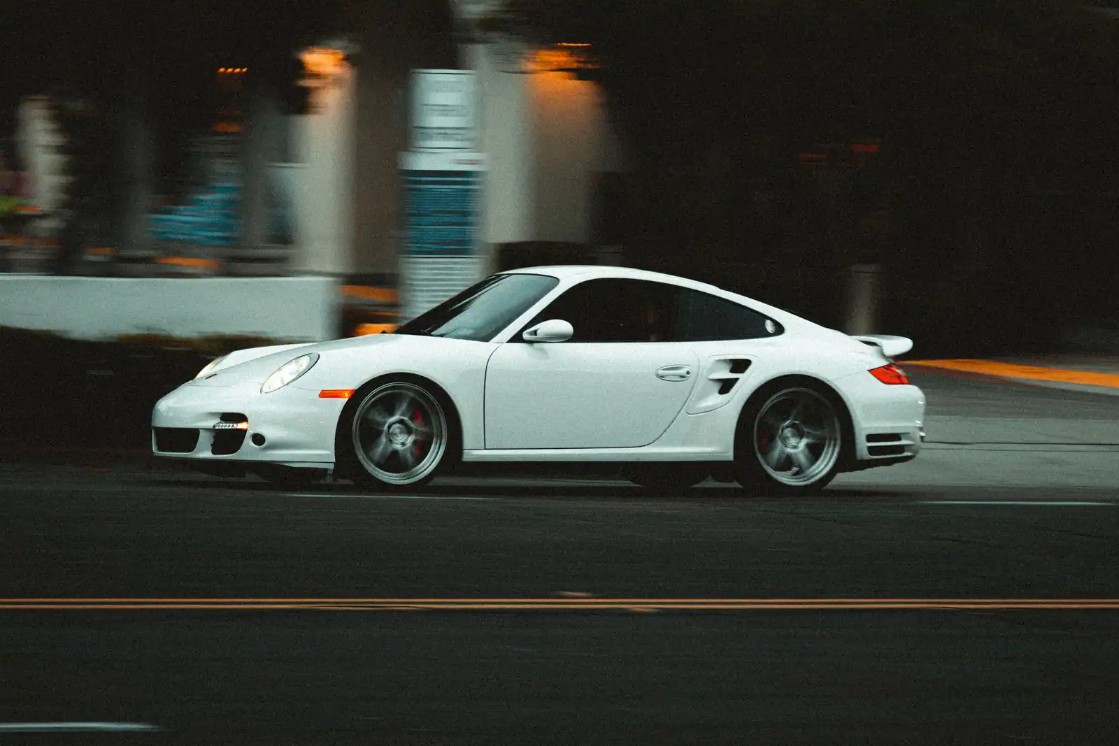 Porsche 911 blanche lancée sur une route au crépuscule, évoquant la location d’une sportive de prestige.