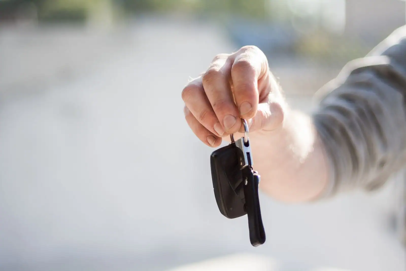 Une main tend une clé de voiture, évoquant la remise des clés lors d'une location.