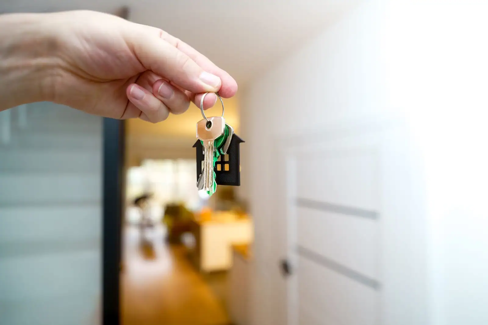 Main tenant un trousseau de clés avec un porte-clés en forme de maison, devant l'entrée d'un logement