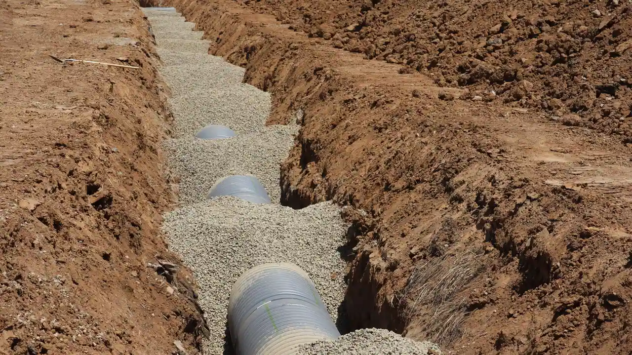 Tranchée ouverte avec son lit de gravier et une canalisation posée au fond, sur un chantier de réseaux