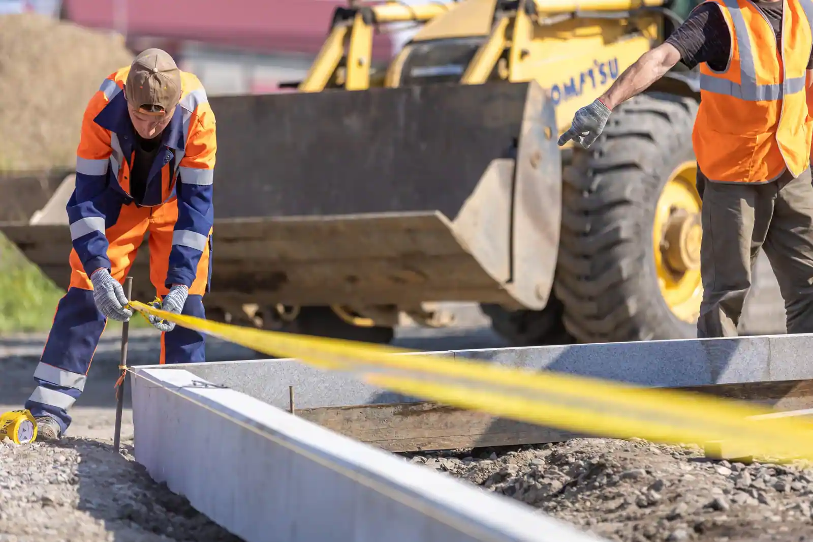 Deux ouvriers relèvent une cote au mètre ruban le long d'éléments béton préfabriqués, sur un chantier
