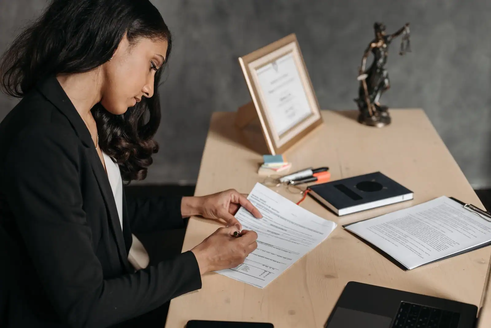 Femme en tailleur relisant un document à son bureau, statuette de la Justice posée à l'arrière-plan