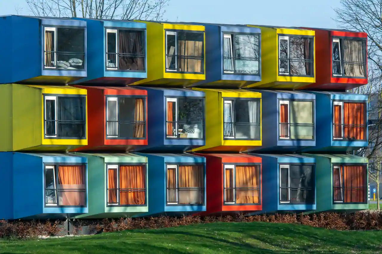 Des logements modulaires empilés sur trois niveaux, chaque module formant un volume coloré distinct.