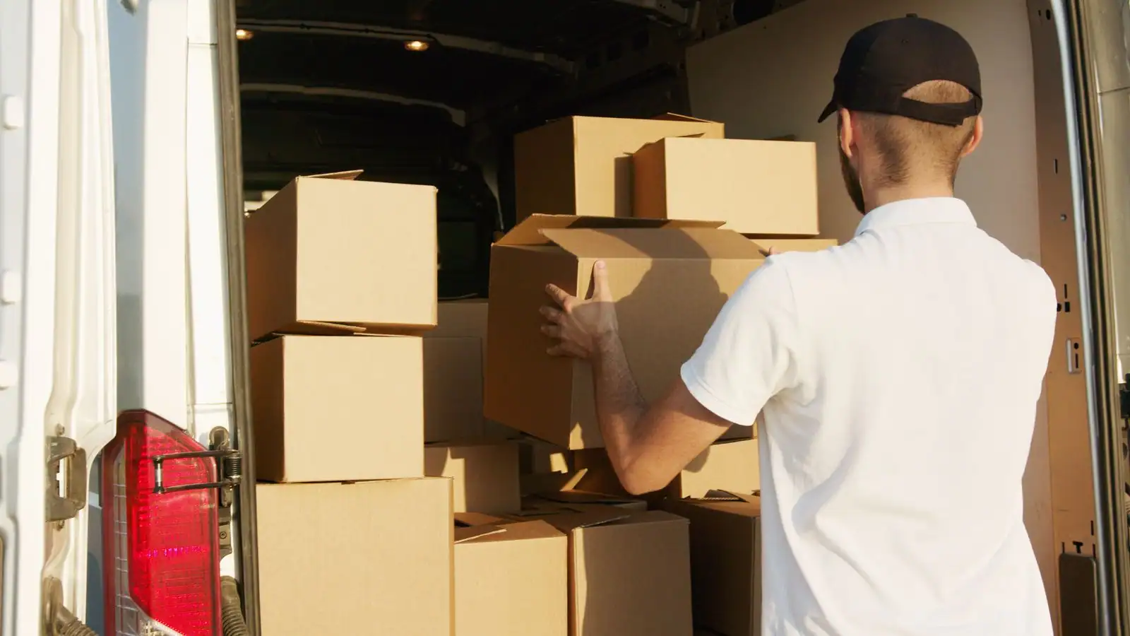 Homme empilant des cartons de déménagement à l'arrière d'un fourgon utilitaire blanc