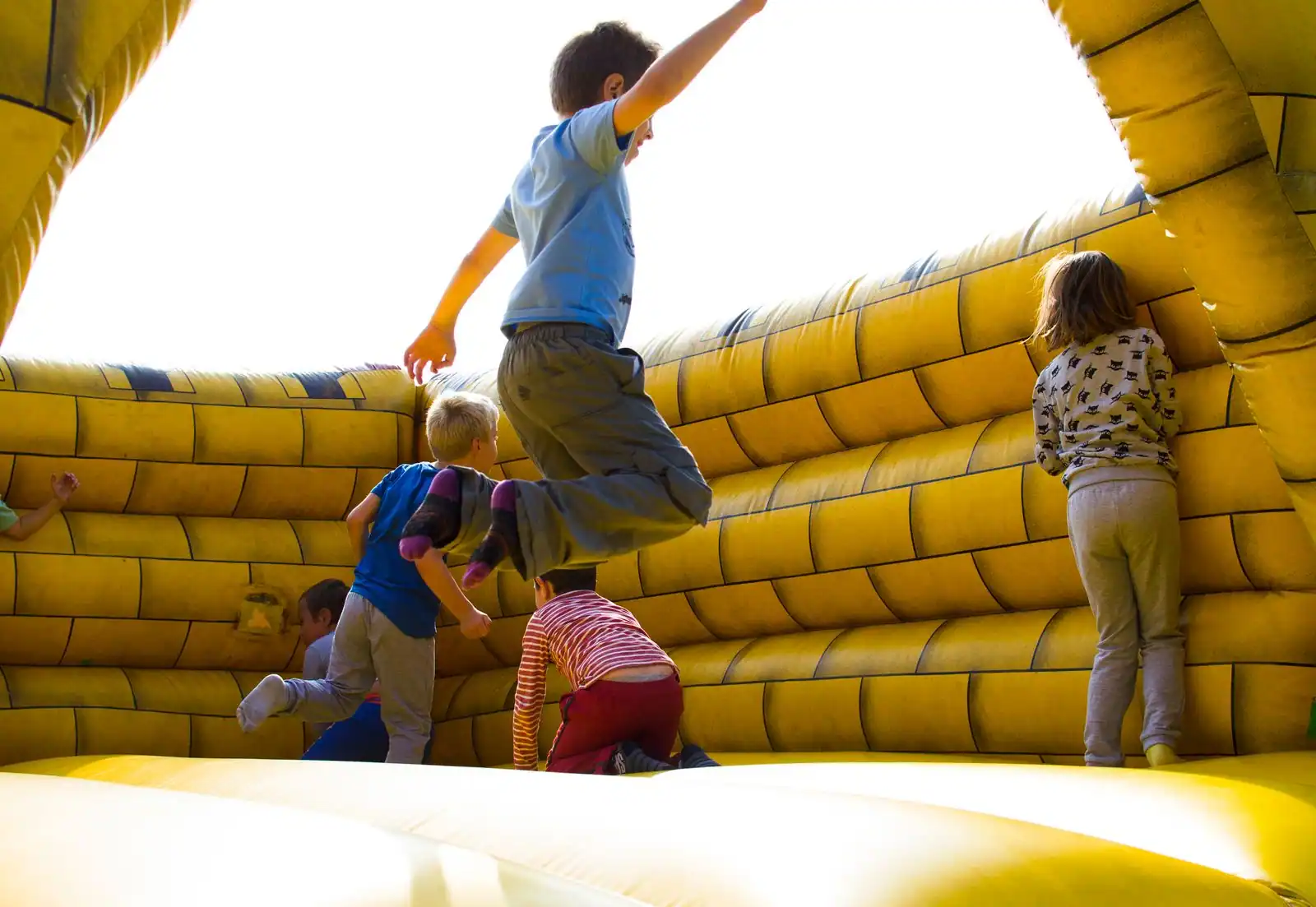 Plusieurs enfants sautent à l’intérieur d’un château gonflable jaune, vue prise depuis l’aire de saut.