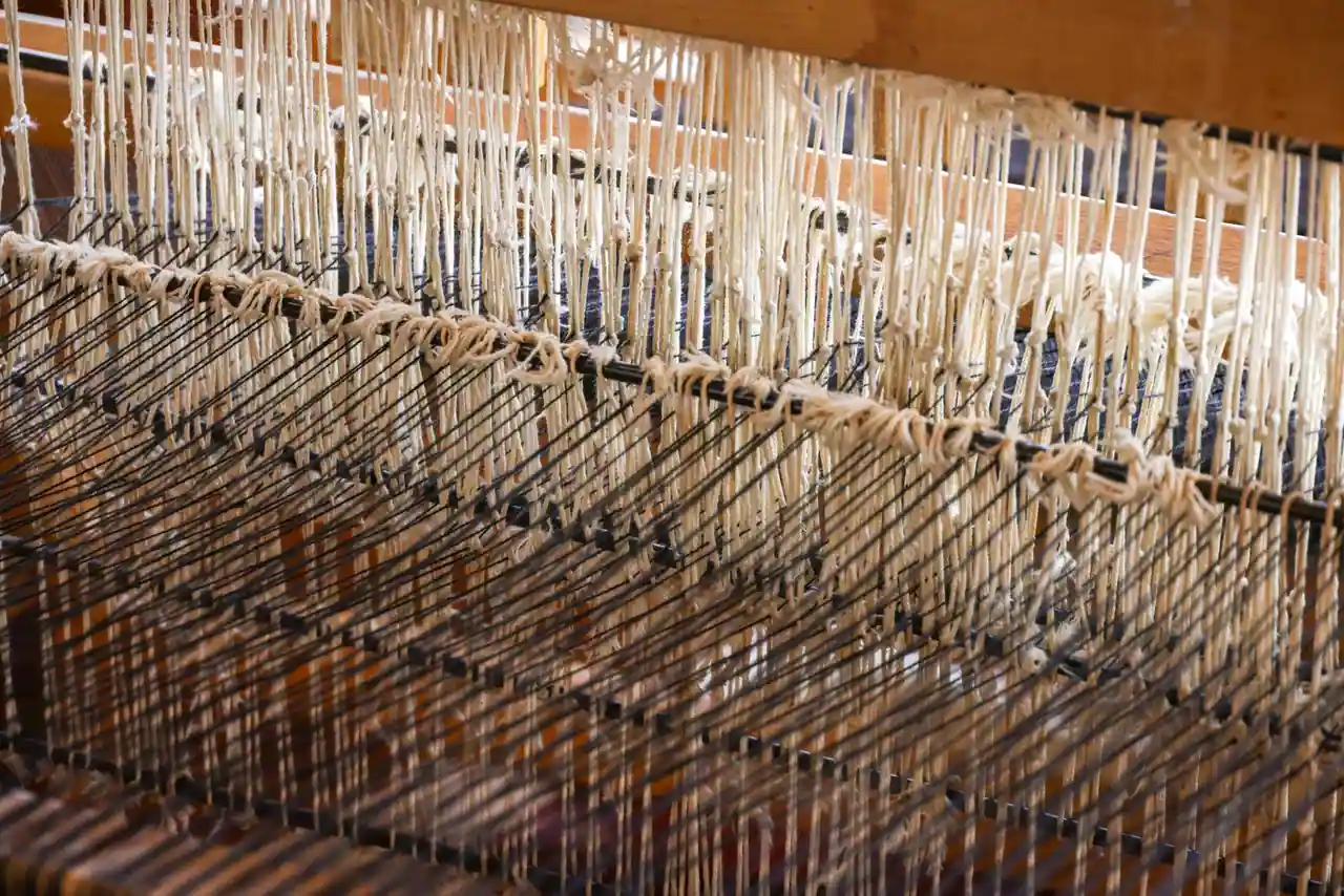 Gros plan sur un métier à tisser en bois, fils de chaîne écrus tendus entre les lisses