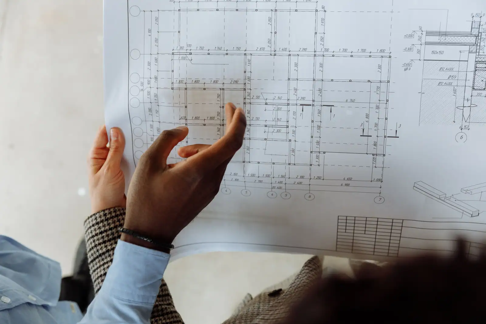 Mains tenant un plan d'architecte coté au millimètre, l'index posé sur le tracé d'une pièce
