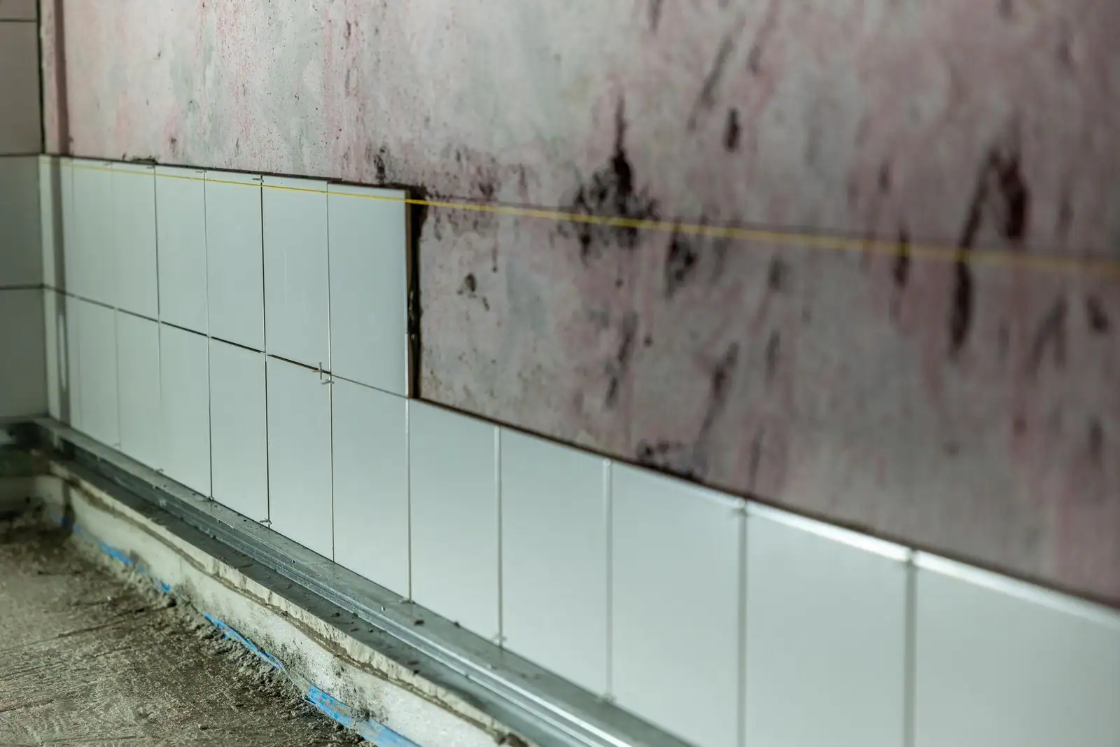 Faïence blanche en cours de pose sur un mur brut, avec cordeau tendu et croisillons, sur un chantier